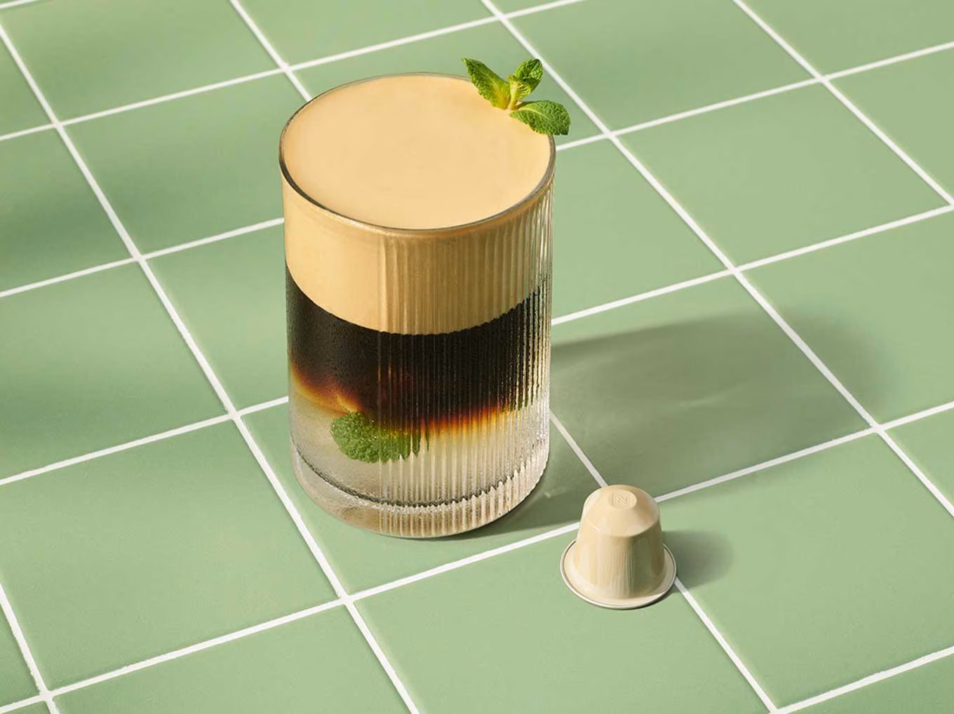 Nespresso Barista Creations Coconut Vanilla Over Ice coffee capsule next to a glass of iced coffee