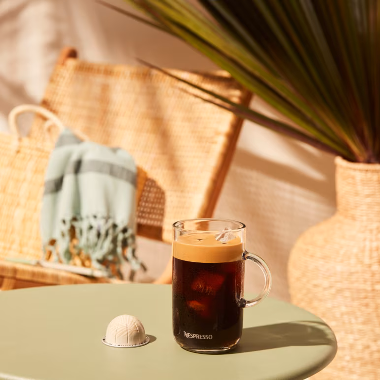 Nespresso Barista Creations Coconut Vanilla Over Ice coffee capsule next to a glass of iced coffee